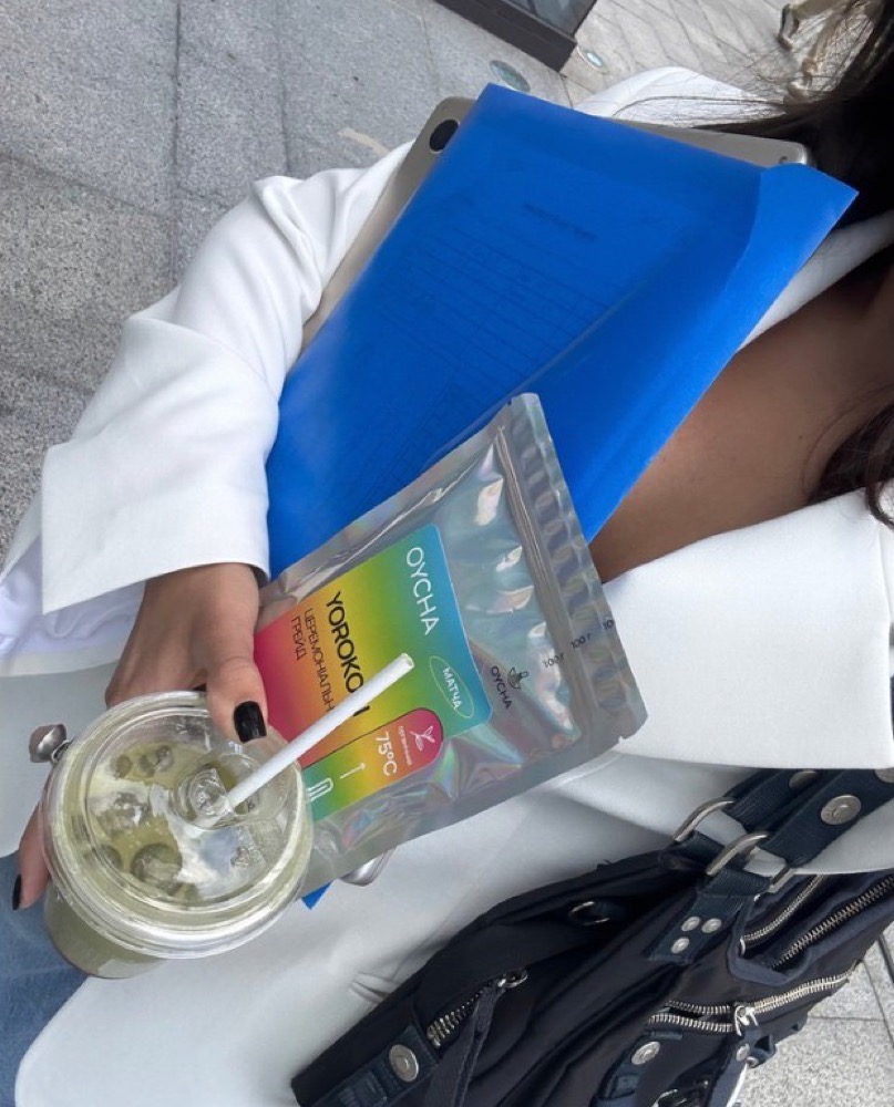 Boisson glacée et sachet OYCHA tenus au-dessus d'un sac posé au sol.